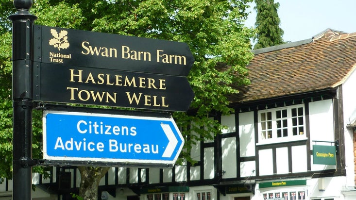 A black metal fingerpost sign posting the way to the old Haslemere well, which used to supply the local area and charged a ha'penny per bucket.